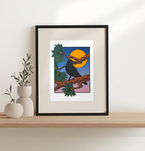 Load image into Gallery viewer, Framed blockprint featuring a raven on pine branches with a full moon and dusk sky behind. Frame sits on a wood shelf with two vases with plants beside it. 
